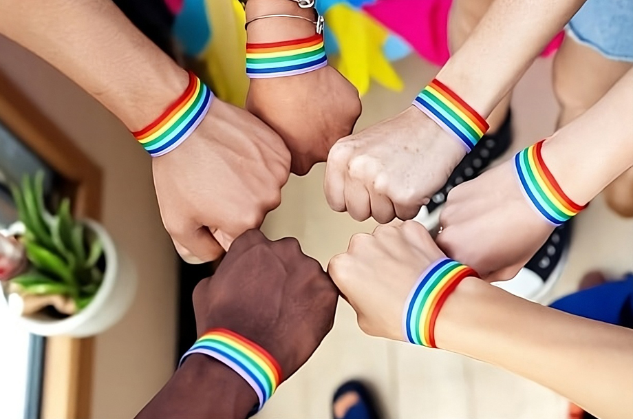 Un grupo de personas chocando puños en señal de hermandad con pulseras del Orgullo en sus muñecas